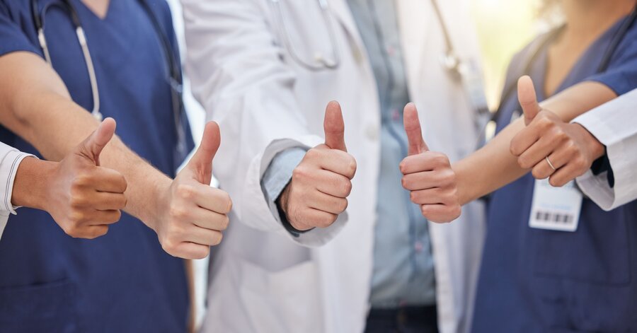 Eine Gruppe von Ärzten, die lächeln und die Daumen nach oben strecken, vermittelt eine positive und unterstützende Atmosphäre in einem Gesundheitszentrum.