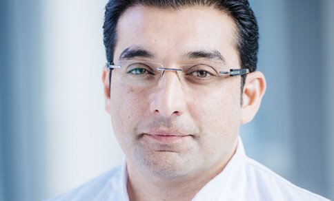 Ein Mann (PD Dr. med. Abdul Shokor Parwani) mit Brille und weißem Arztkittel lächelt in die Kamera.
