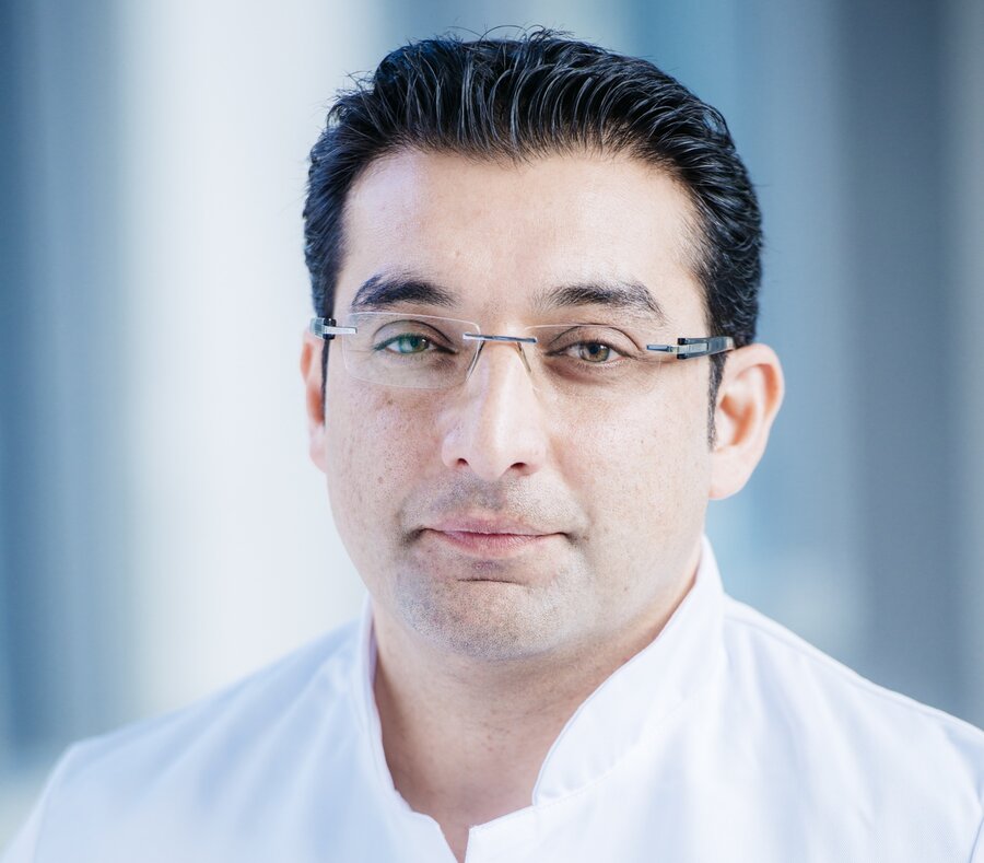 Ein Mann (PD Dr. med. Abdul Shokor Parwani) mit Brille und weißem Arztkittel lächelt in die Kamera.