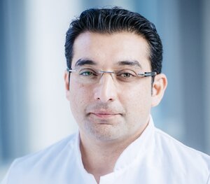 Ein Mann (PD Dr. med. Abdul Shokor Parwani) mit Brille und weißem Arztkittel lächelt in die Kamera.