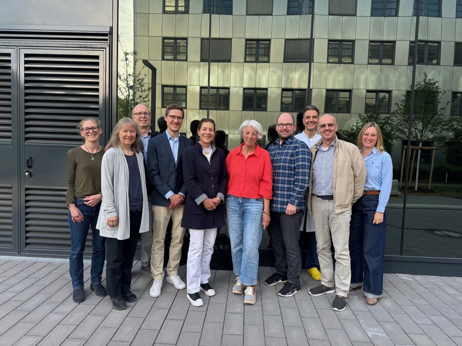  A group of 10 people are standing in front of a building, smiling. The atmosphere is friendly.