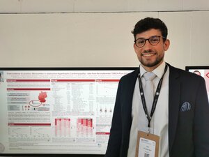 Photo of Dr Jan Kölemen standing in front of his scientific poster at the ESC Congress, titled "From evidence to practice: Mavacamten in obstructive Hypertrophic Cardiomyopathy – data from the multicenter TORCH-Plus-DZHK21". He is wearing glasses, a dark suit, light blue tie, and an ESC Congress lanyard with name badge, smiling at the camera.