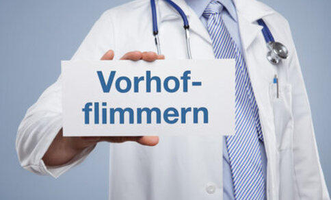 Ein Arzt hält eine Karte in der Hand, auf der „Vorhofflimmern“ steht.
