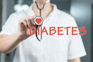 A person in a white coat holds a stethoscope with a heart symbol on it. The word "DIABETES" is written in red across the image, suggesting a medical focus.