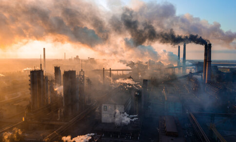 Aerial view of an industrial area at sunset, with several factories emitting thick, dark smoke. 