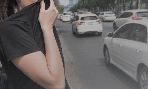  A person holds their T-shirt in front of their mouth and nose while standing on a busy street to protect themselves from air pollution.
