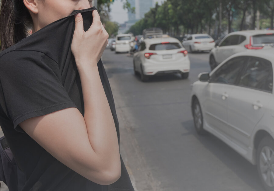  A person holds their T-shirt in front of their mouth and nose while standing on a busy street to protect themselves from air pollution.