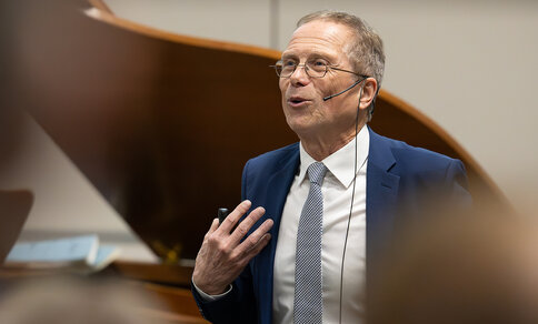A man in a suit and tie, identified as Prof. Dr Gerd Hasenfuß, speaks during his farewell lecture on 18 October 2024 in Göttingen. He gestures with one hand and wears a headset microphone. 