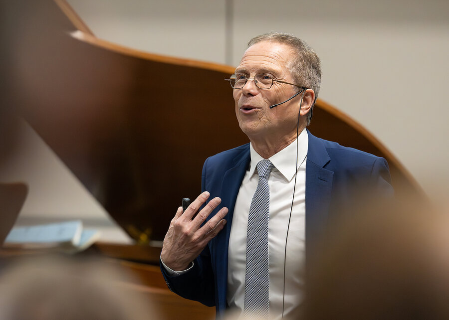 A man in a suit and tie, identified as Prof. Dr Gerd Hasenfuß, speaks during his farewell lecture on 18 October 2024 in Göttingen. He gestures with one hand and wears a headset microphone. 
