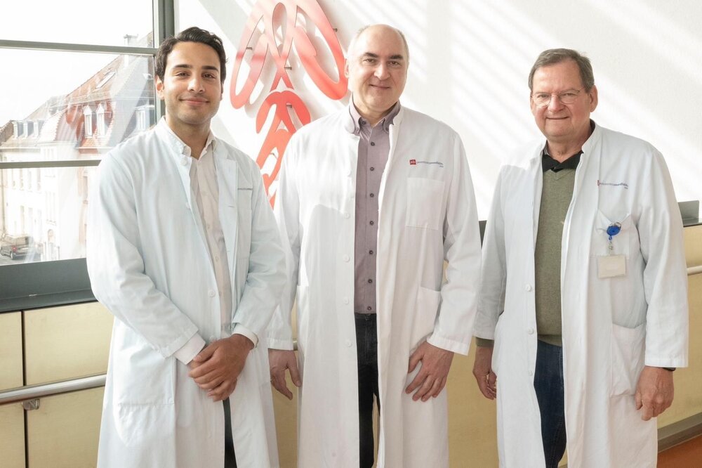 Three men in white lab coats smile at the camera.