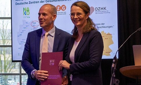 Zwei Personen in Geschäftskleidung halten ein Dokument in der Hand. (Prof. Uwe Reuter und Wissenschaftsministerin Bettina Martin) 