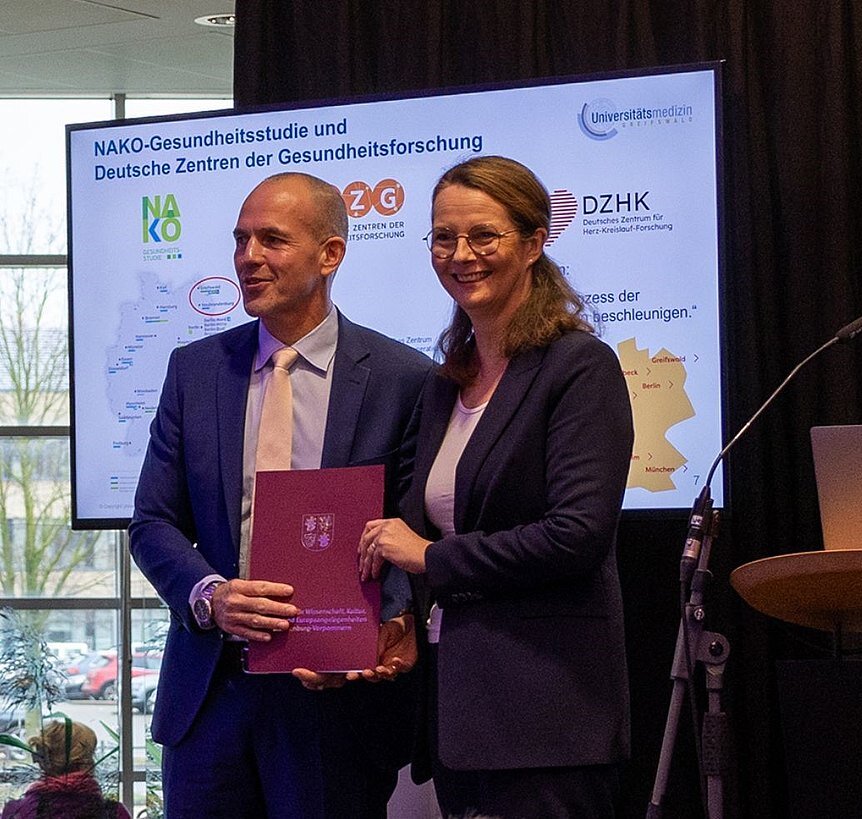 Two people in business attire holding a document. (Prof Uwe Reuter and Minister of Science Bettina Martin) 