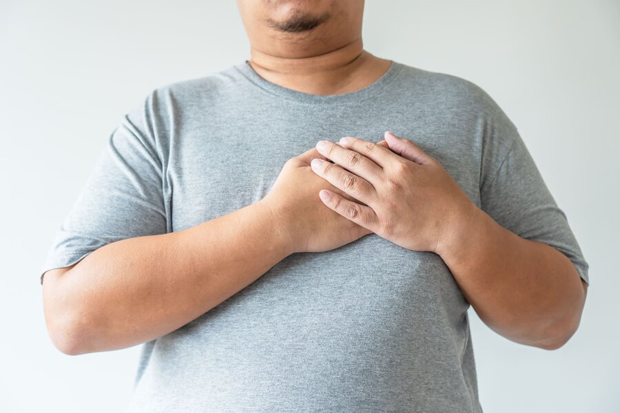 A person in a gray t-shirt places both hands over their chest, conveying concern or discomfort. 