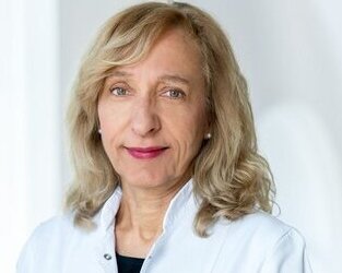a woman in a lab coat who smiles warmly at the camera.
