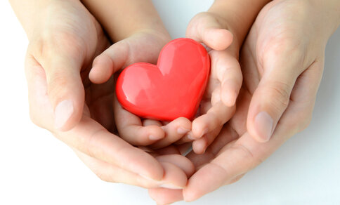 An adult and a child hold a heart in their hands.