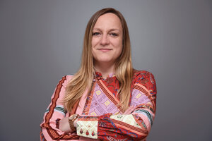 Portrait photo of Prof Daniela Panáková, smiling and looking into the camera with her arms crossed. She is wearing a colourful, patterned top and a wristwatch. Her blonde hair falls loosely over her shoulders and the background is a neutral grey. 