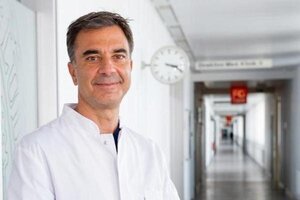 A man (Prof. Dr Steffen Massberg) is standing in a corridor wearing a lab coat and looking friendly at the camera.