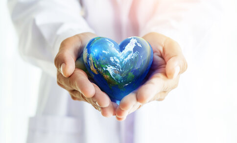 A person in a white doctor's coat holds a heart-shaped earth in his hands. 