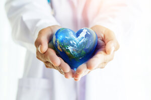 A person in a white doctor's coat holds a heart-shaped earth in his hands. 