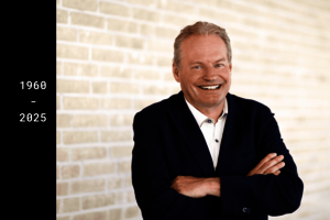  A man in a suit, identified as Professor Thomas Wieland, stands with his arms loosely crossed in front of a bright background and smiles warmly.