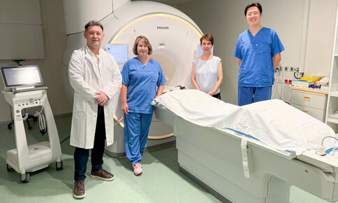 Four medical professionals stand in front of an MRI machine in a hospital room. 