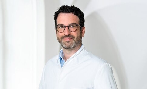  A man in a white lab coat smiling warmly at the camera.