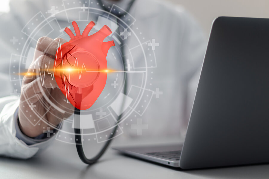  A doctor or scientist holds a stethoscope to a digital, holographic image of a heart. The image shows an ECG line that symbolises the heartbeat. A laptop is visible in the background, indicating the use of modern technologies and digital medicine. Surrounding the heart are symbols symbolising medical research and cardiovascular health.