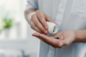 A close-up of a person wearing a light grey shirt, holding a small white medicine bottle and pouring tablets into their open hand.