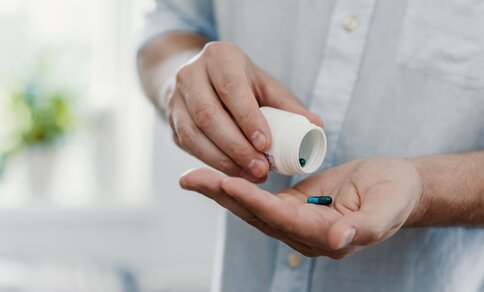 A close-up of a person wearing a light grey shirt, holding a small white medicine bottle and pouring tablets into their open hand.