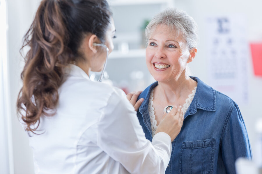 An elderly woman is listened to with a stethoscope on her chest during a medical examination - symbolic image for cardiovascular care in women.