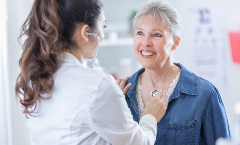 An elderly woman is listened to with a stethoscope on her chest during a medical examination - symbolic image for cardiovascular care in women.