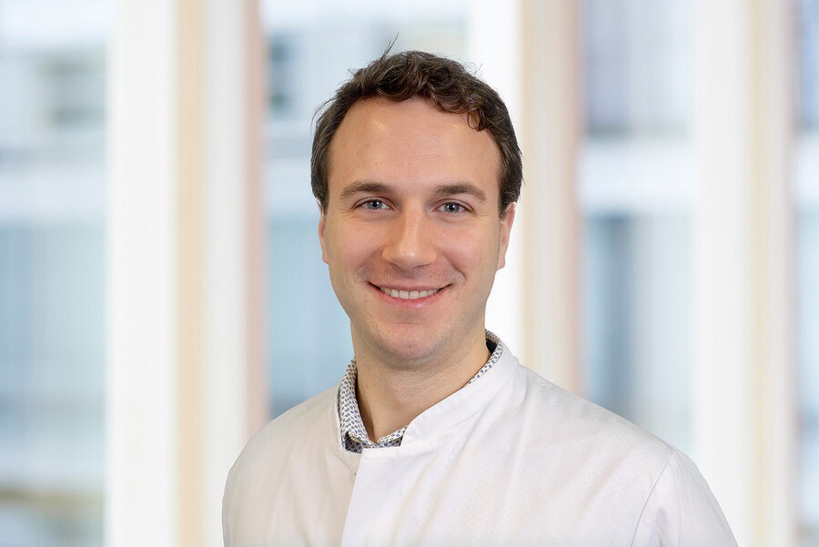 Ein Mann in einem weißen Arztkittel, identifiziert als Dr. Sören Brandenburg, lächelt freundlich in die Kamera. 