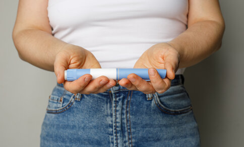 Person holding a medicine pen in both hands, wearing a white top and blue jeans.