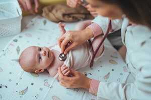 A doctor examines a calm baby with a stethoscope on a cute, patterned blanket. 