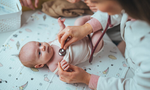 Ein Arzt untersucht ein ruhiges Baby mit einem Stethoskop auf einer niedlichen, gemusterten Decke. 