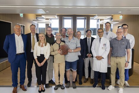 A group of women and men are standing in a modern interior for a group photo. They are standing side by side and smiling at the camera
